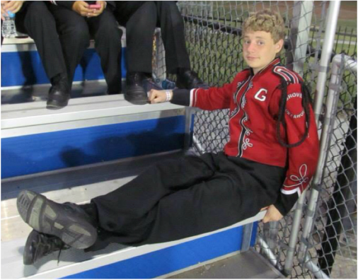 Picture of a blonde teen boy in a Marching Band uniform resting on a bleacher bench
