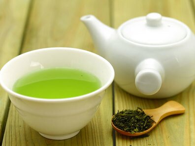 Picture of a cup of Green Tea, a Teapot and a wooden spoon filled with dry tea leaves