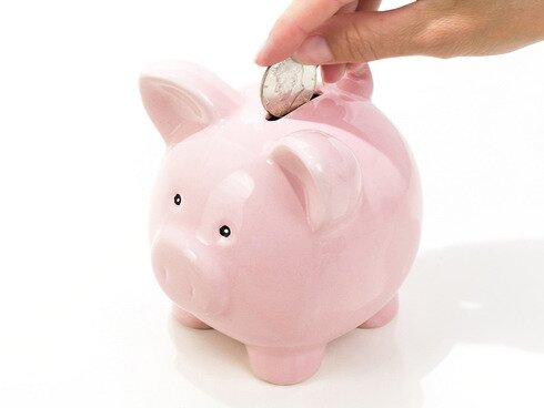 Picture of a pink piggy bank and a woman's hand dropping a coin in
